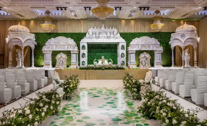 White mandapam stage with green hedge wall, floral aisle and white chairs